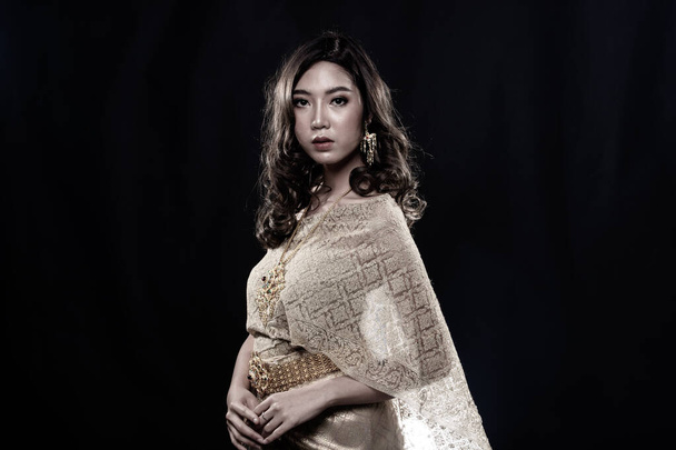 Goldenes Kleid der thailändischen Tracht oder südostasiatisches Gold Kleid in asiatischer Frau mit Dekoration stehen in vielen Posen unter dunkelschwarzem Hintergrund Kopierraum mit Rauch-Porträt - Foto, Bild