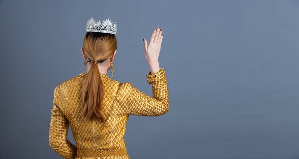 Miss missverkiezing Diamond kroon van Thai Traditioneel Kostuum of Zuidoost-Azië goud Jurk in Aziatische vrouw met decoratie pose golf hand terug te draaien portret onder Studio verlichting grijze achtergrond - Foto, afbeelding