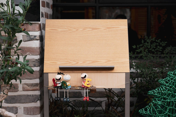 Tablero de panel de menú de madera con decoraciones de muñecas fuera de un restaurante
. - Foto, imagen