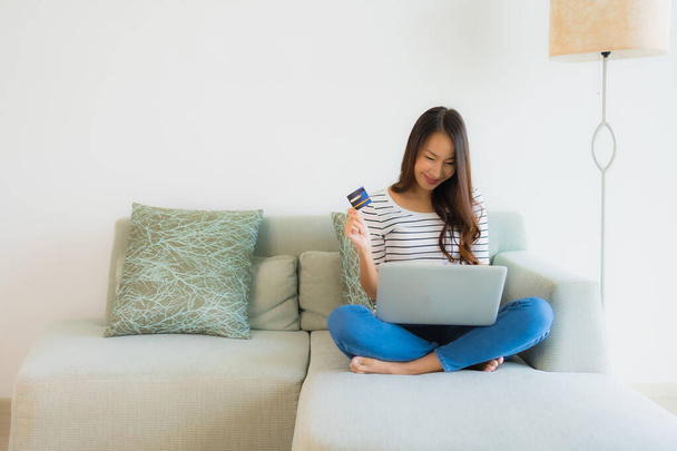 Retrato bonito jovem asiático mulheres com cartão de crédito celular ou computador para compras on-line no sofá na sala de estar interior
 - Foto, Imagem