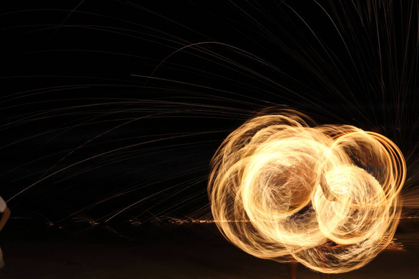High Skill Man speelt vuurwerk door spinnen hout paal met stookolie en vuur, cirkel rond als ring van vuur op het strand langs de oceaan in tropische eiland, lange blootstelling wazig beweging - Foto, afbeelding
