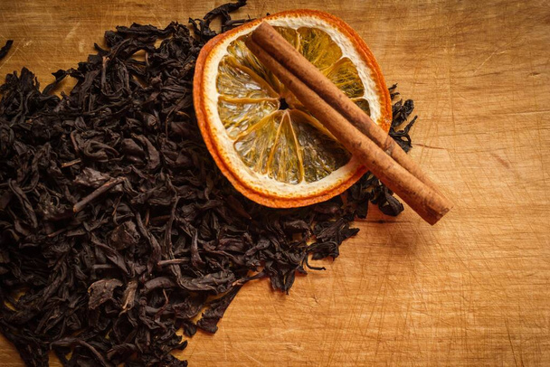 Old, wooden, kitchen table, top of the leaves of dry black tea, cinnamon and orange. Warmth, comfort, home cooking. Warm tones, vignetting. - Photo, Image
