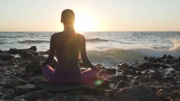 日没時の海側における女性の練習瞑想の背面ビュー - 映像、動画