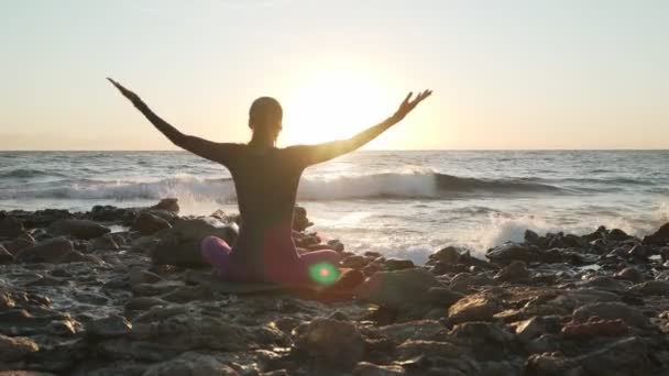 Vista posterior de la mujer se sienta en namaste pose meditando en la playa al atardecer
 - Metraje, vídeo