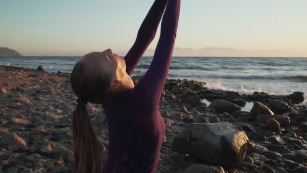 Jovem mulher senta-se em postura namaste meditando ao lado do mar ao pôr do sol
 - Filmagem, Vídeo