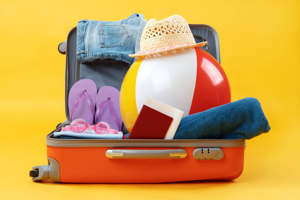 Open full suitcase with items for relaxation on a yellow background. - Foto, Bild