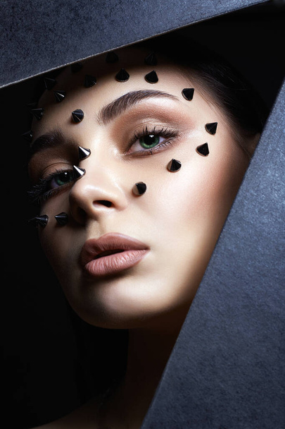 beautiful girl with steel spikes on her Face. Beautiful woman face with Make-up inside the hole of black paper. Beauty Portrait - Foto, Imagen