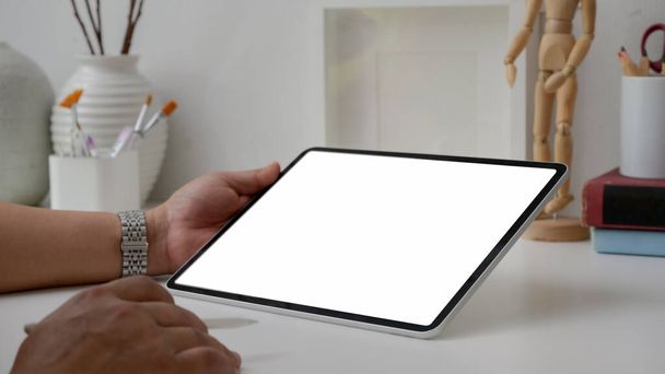 Обрезанный снимок мужчины-художника, работающего на пустом экране планшета со стилусом ручкой, инструментами для рисования и украшениями на белом столе на минимальном рабочем месте
  - Фото, изображение