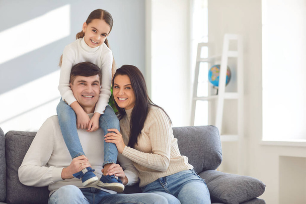 Happy smiling family. Daughter sits on fathers shoulders with mother sitting on the sofa - Foto, Imagem