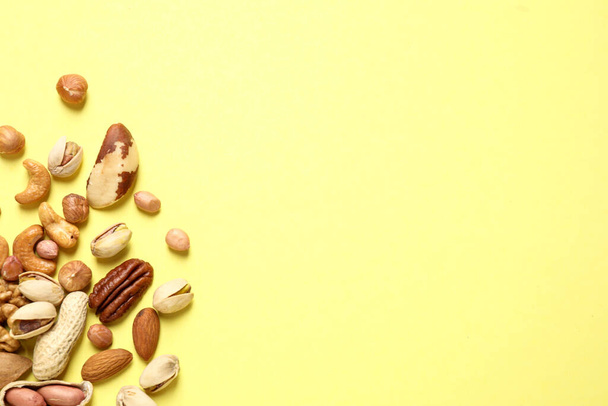 Different delicious nuts on yellow background, flat lay. Space for text - 写真・画像
