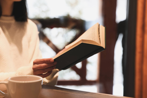 Woman with coffee reading book at wooden table, closeup - Foto, Imagen