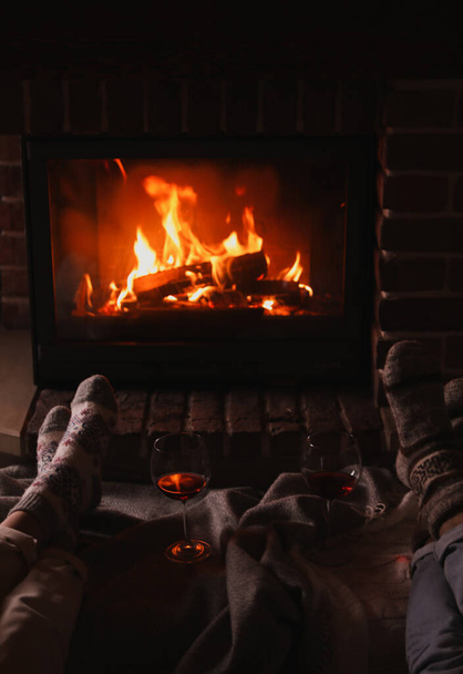 Couple and glasses of red wine near burning fireplace, closeup - Фото, изображение