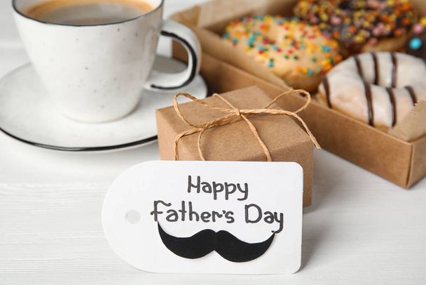 Label met zin HAPPY FATHER 'S DAY, donuts, koffie en cadeau op witte houten tafel - Foto, afbeelding