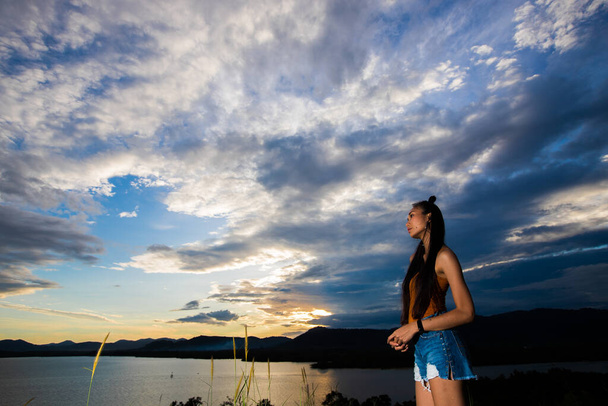 Open World Sky with wind Cloud over sunset red ray beam to young adult asian woman long black hair skinny vast who feel lonely happy success to stand on top of clip ocean sight view, copy space - Photo, Image