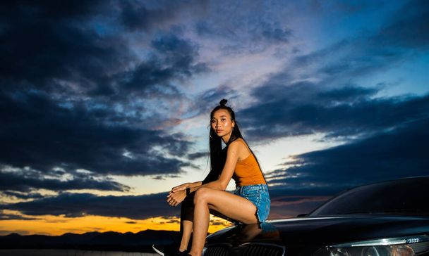 若い大人のアジアの女性に日没の赤い線ビームの上に風の雲とオープン世界の空長い黒い髪のスキニー広大な孤独な幸せな成功を感じる人は、スポーツカーに座って、表現をリラックスし、スペースをコピー - 写真・画像