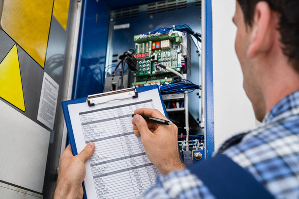 Cropped Image Of Male Electrician Holding Clipboard While Examining Fusebox - Photo, Image