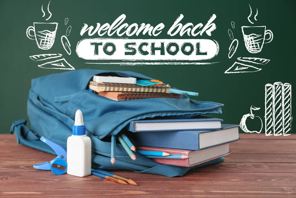 Backpack and stationery on table near blackboard with text WELCOME BACK TO SCHOOL - Photo, Image