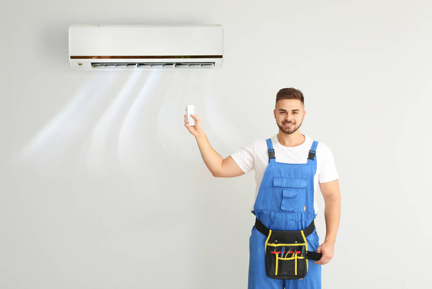 Άνδρας τεχνικός ενεργοποιεί το κλιματιστικό στον ελαφρύ τοίχο - Φωτογραφία, εικόνα