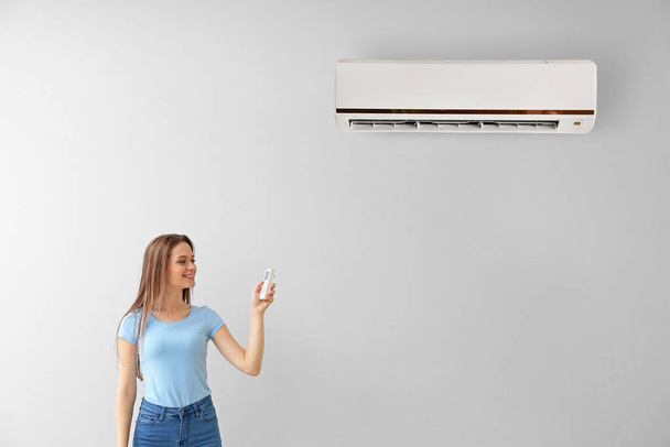 Jonge vrouw schakelt airconditioner op lichtmuur in - Foto, afbeelding