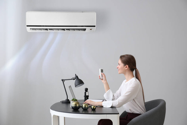 Young woman switching on air conditioner in office - Photo, Image