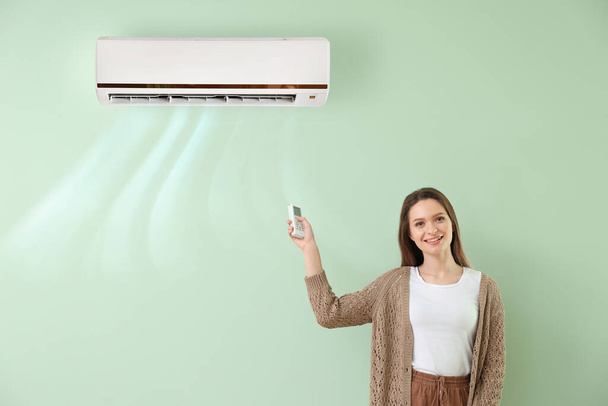 Young woman switching on air conditioner on color wall - Photo, Image
