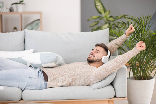 Молодий чоловік слухає музику, лежачи на дивані вдома
 - Фото, зображення
