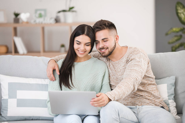 Young couple with laptop sitting on sofa at home - Photo, Image