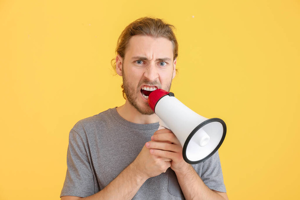 schreiender junger Mann mit Megafon auf farbigem Hintergrund - Foto, Bild