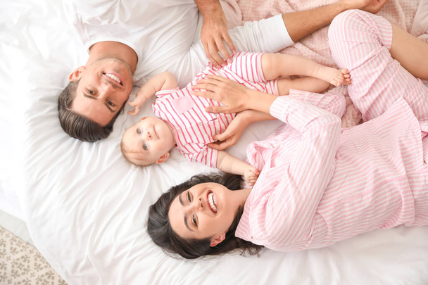 Leuke baby met ouders liggend op bed, bovenaanzicht - Foto, afbeelding
