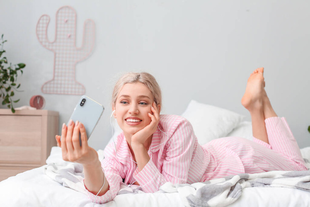 Jovem mulher tomando selfie enquanto ouve música no quarto
 - Foto, Imagem