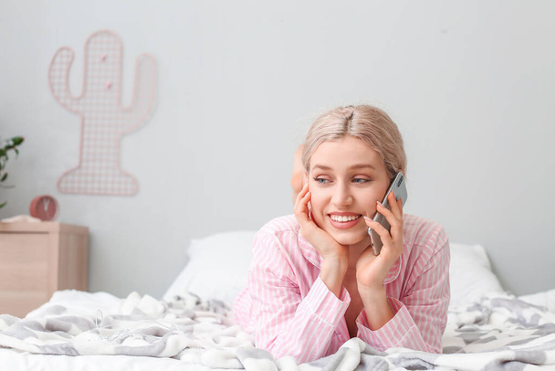 Yatak odasında cep telefonuyla konuşan genç bir kadın. - Fotoğraf, Görsel