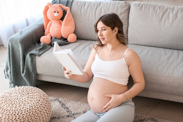 Beautiful pregnant woman reading book at home - Valokuva, kuva