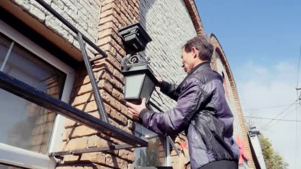 elektricien staande op een ladder en verandering de gloeilamp in huis gevel lamp - Video