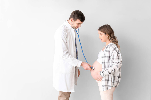 Doctor examining pregnant woman against grey background - Photo, Image