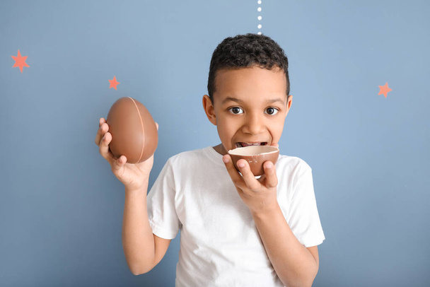 Roztomilý africko-americký chlapec se sladkými čokoládovými vejci na barevném pozadí - Fotografie, Obrázek