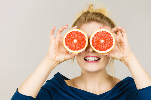 Healthy diet, refreshing food full of vitamins. Woman holding sweet delicious citrus fruit, grapefruit two halfs pretending it is eyeglasses - Фото, зображення