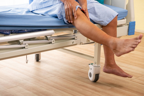 Ασιάτης ασθενής αισθάνεται πόνο στο γόνατό του στο δωμάτιο του νοσοκομείου. - Φωτογραφία, εικόνα