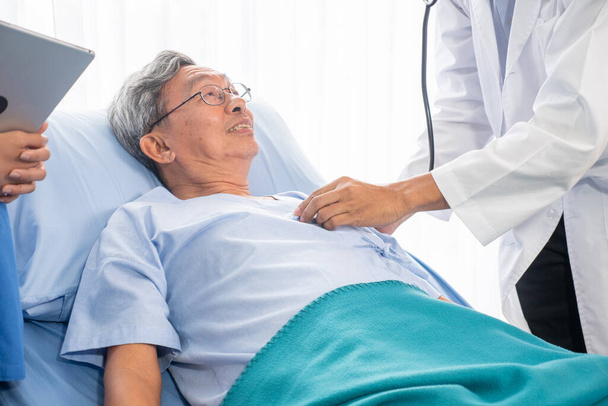 Lekarz auscultating dla azjatyckich mężczyzn za pomocą stetoskopu w pokoju szpitalnym - Zdjęcie, obraz
