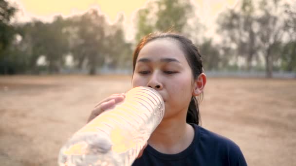 Ασιάτισσα νεαρή γυναίκα πίνει νερό από πλαστικά μπουκάλια αφού έκανε τζόκινγκ στο πάρκο. Χάσε βάρος. Υγιεινός τρόπος ζωής. - Πλάνα, βίντεο