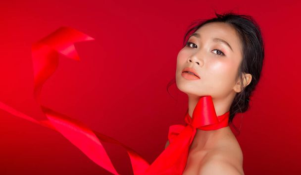 Portret moda Azji Czarne włosy garbowana skóra kobieta z silnym kolorem czerwone usta, studio oświetlenie czerwone czerwone tło przestrzeń kopia, dziewczyna wiąże łuk czerwona wstążka i wiatr cios, selektywne skupienie - Zdjęcie, obraz
