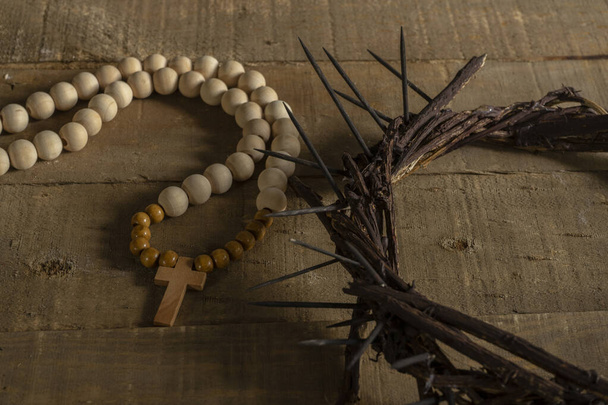 Concept of passion, crucifixion and resurrection. Iconic symbols related to Palm Sunday and Easter rest on a wooden table, crown of thorns and a rosary. - Photo, Image