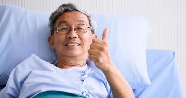 Mężczyzna uśmiechnięty i leżący na łóżku w szpitalu. - Zdjęcie, obraz