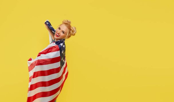 American girl. Happy young woman in denim clothes holding USA flag isolated on yellow background - Фото, изображение