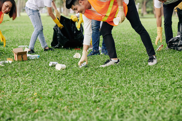 Young volunteers wearing bright vests and rubber gloves when collecting garbage in park - Valokuva, kuva