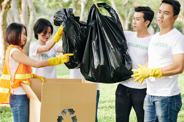 Молодые волонтеры складывают полные мешки мусора в картонные коробки после прогулки в парке - Фото, изображение