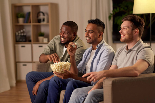 male friends with popcorn watching tv at home - Photo, Image
