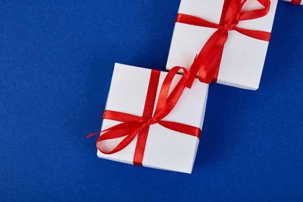 Luxus weiße Geschenkboxen mit rotem Band auf blauem Hintergrund in Trendfarbe. Valentinstag, Weihnachten, Geburtstagsgeschenke. Mutter- oder Frauentag. flach lag. Kopierraum. Ansicht von oben. - Foto, Bild