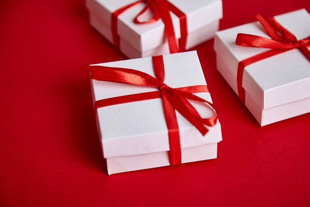 Πολυτελή λευκά κουτιά δώρου με κόκκινη κορδέλα σε κόκκινο φόντο. Ημέρα του Αγίου Βαλεντίνου, Χριστούγεννα, δώρα γενεθλίων. Ημέρα Μητέρας ή Γυναίκας. Επίπεδη. Αντιγραφή χώρου. Άνω όψη. - Φωτογραφία, εικόνα
