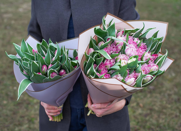 Δύο πλούσια μπουκέτο τουλίπες που πραγματοποιήθηκε από το χέρι μιας γυναίκας σε εξωτερικούς χώρους. Λουλούδια είναι ένα μεγάλο δώρο για διακοπές, γενέθλια, 8 Μαρτίου - Φωτογραφία, εικόνα