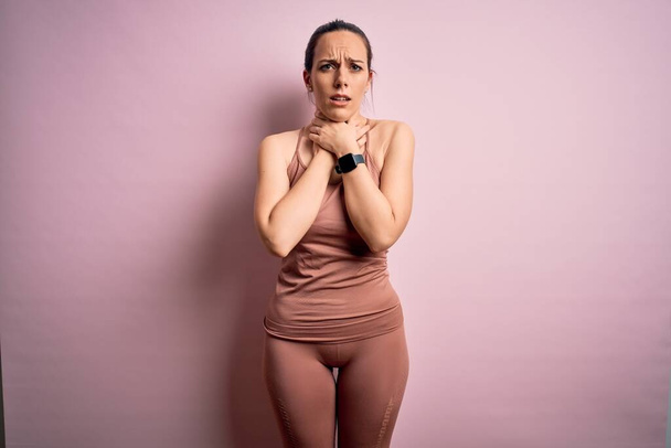 Young blonde fitness woman wearing sport workout clothes over pink isolated background shouting and suffocate because painful strangle. Health problem. Asphyxiate and suicide concept. - Фото, зображення
